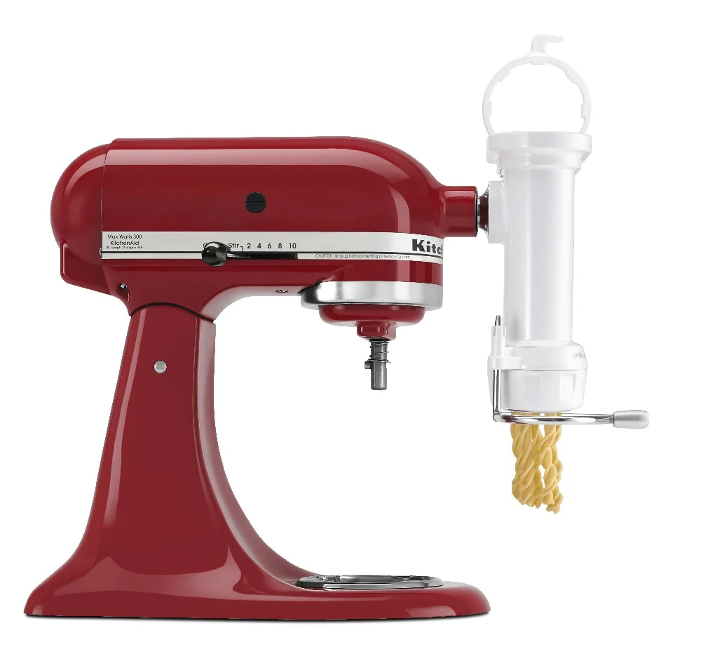Prensa blanca KitchenAid acoplada a una batidora de pie, con tolva superior, manivela lateral y pasta saliendo por la base. - Vista 3